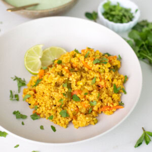 Daliya Pulao served in a bowl with lime wedges and garnished with cilantro
