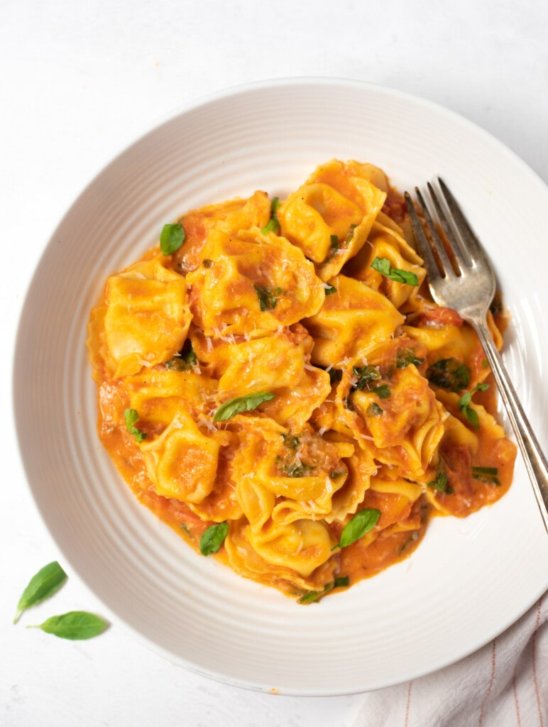 Cheese tortellini in creamy tomato sauce in a bowl topped with basil leaves