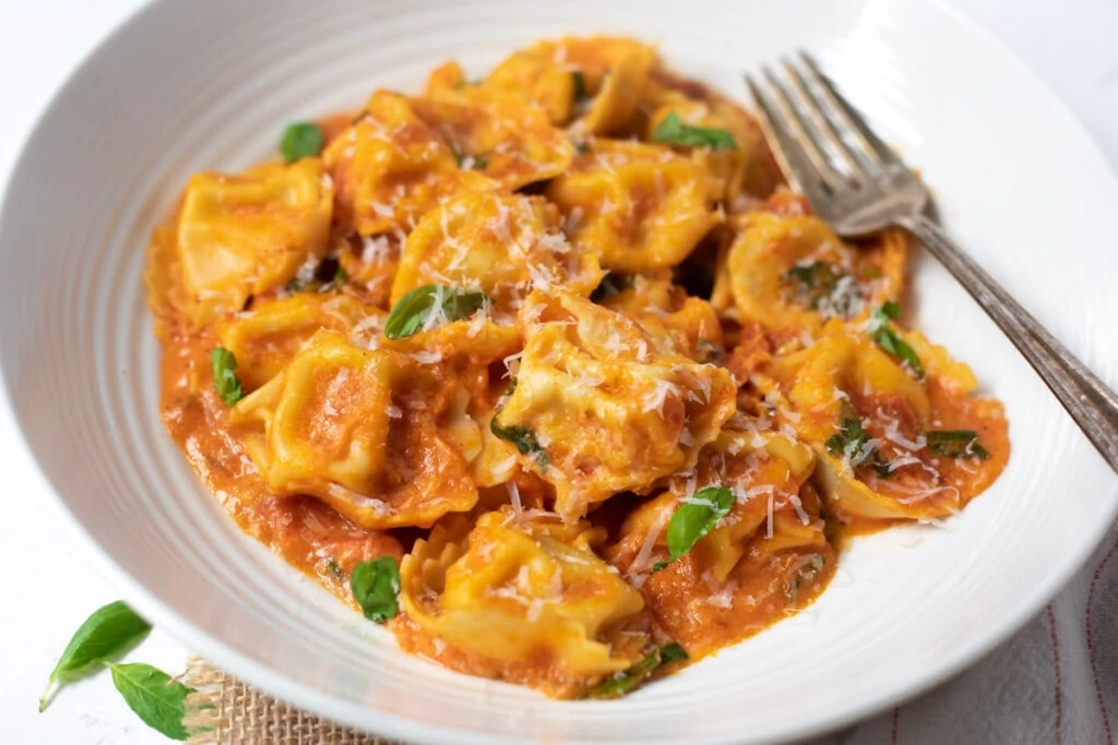 Cheesy Tomato Tortellini served in a bowl topped with basil and parmesan 