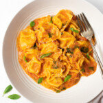 creamy tortellini pasta in a bowl garnished with basil leaves
