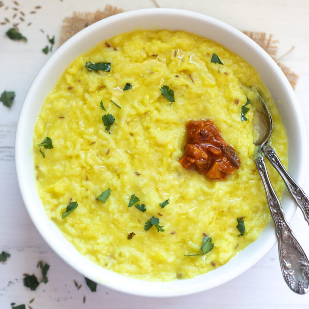 plain khichdi made with moong dal and rice served in a bowl topped with ghee, cilantro and pickle