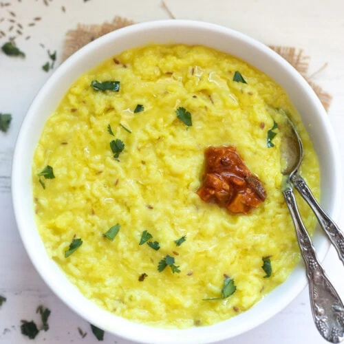 Moong Dal Khichdi in a bowl garnished with cilantro and topped with pickle
