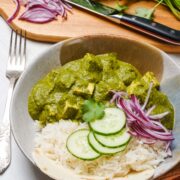 Palak/Saag Tofu curry in a bowl with rice, and side of red onions and cucumber.