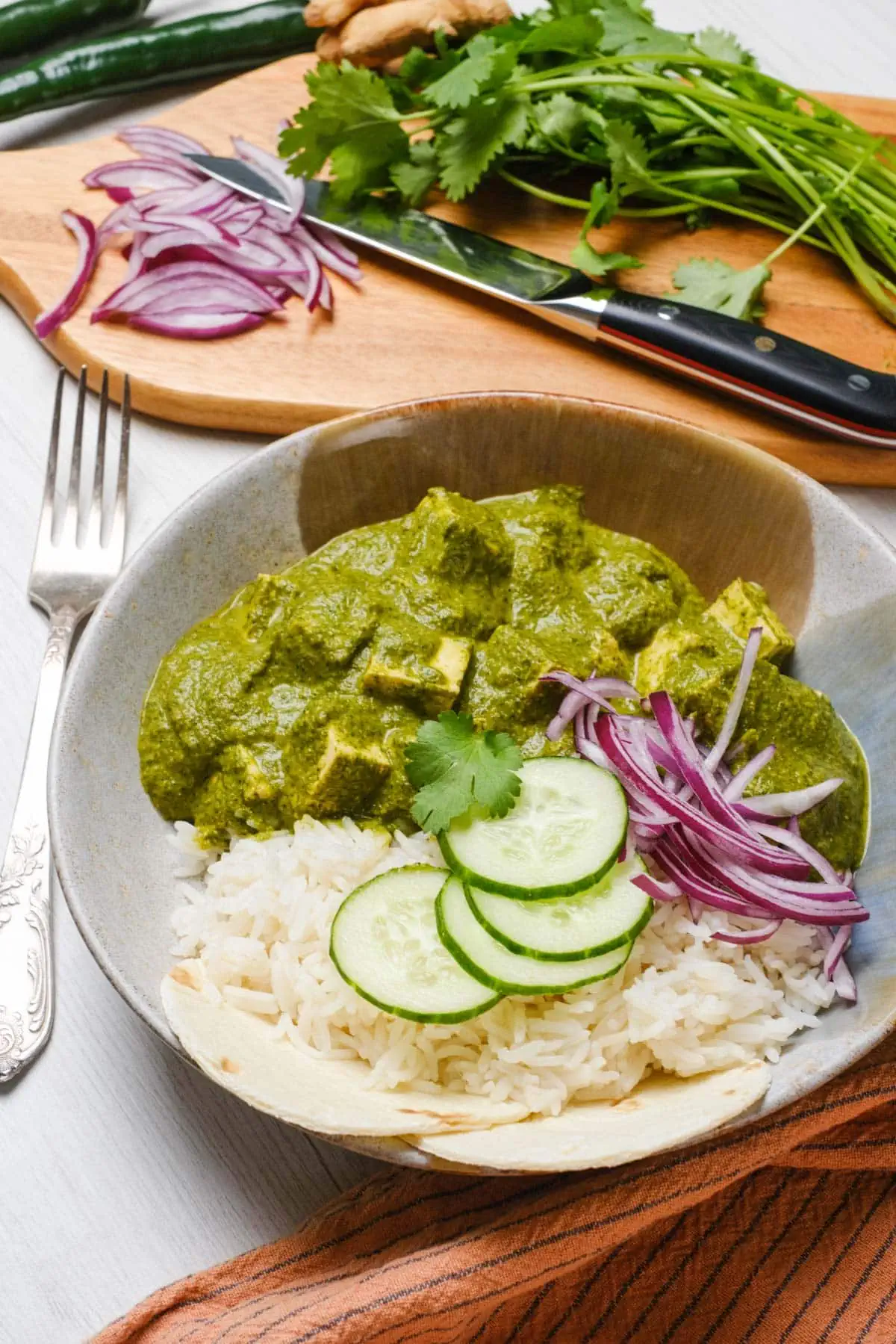 Palak/Saag Tofu curry in a bowl with rice, and side of red onions and cucumber. 