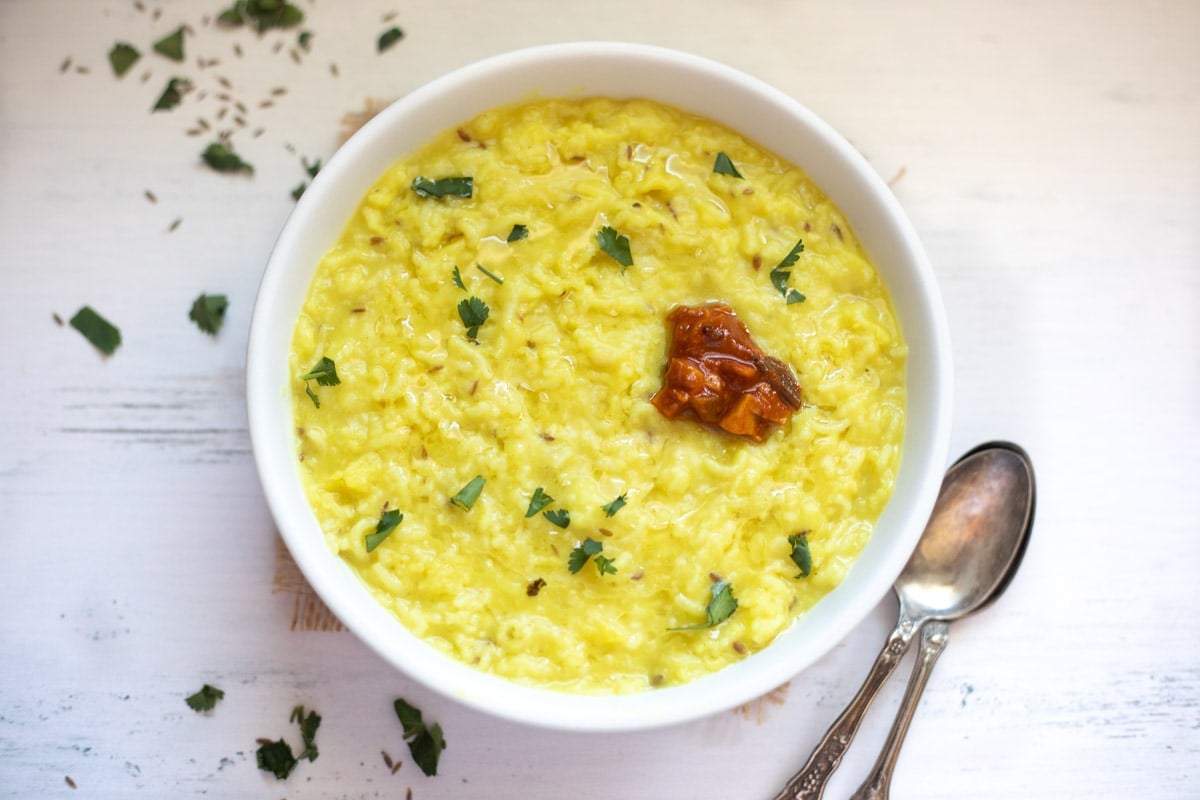 plain khichdi made with moong dal and rice served in a bowl topped with ghee, cilantro and pickle
