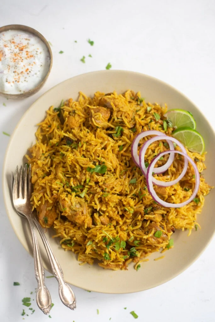 Chicken Biryani served in a plate garnished with onions, lime along with a side of raita
