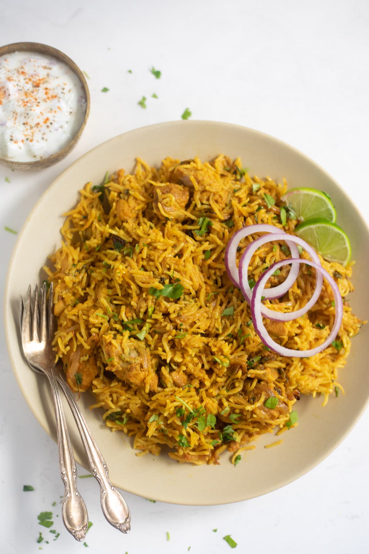 Chicken Biryani served in a plate garnished with onions, lime along with a side of raita