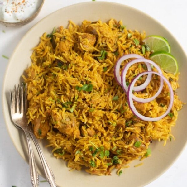 Chicken Biryani served in a plate garnished with onions, lime along with a side of raita