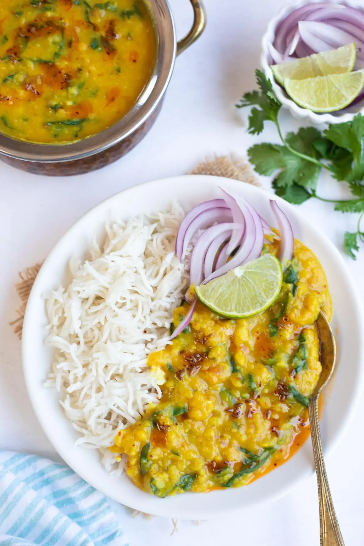 Spinach dal served with rice garnished with onions and lime