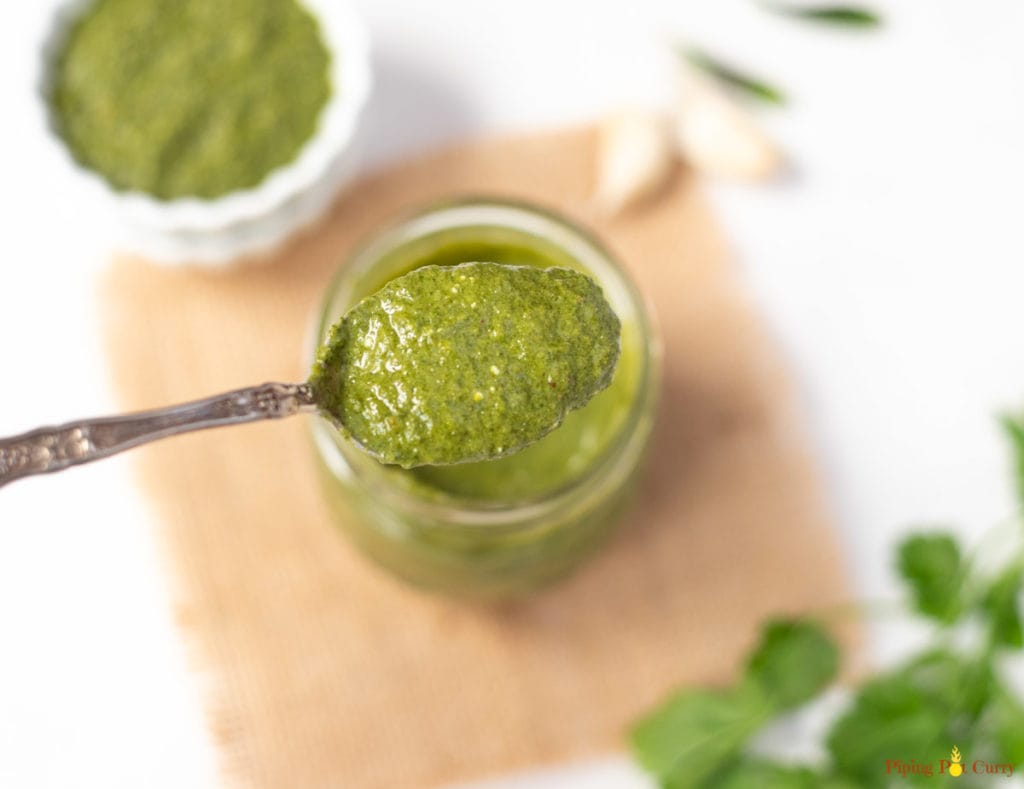 Green mint cilantro chutney in a spoon over a glass jar