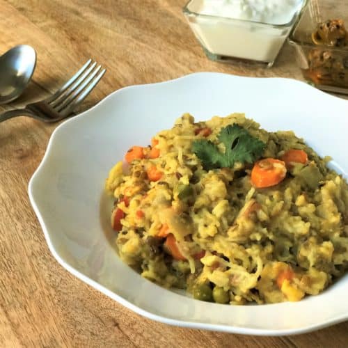 Instant Pot Masala Khichdi in a white bowl along with yogurt and pickle.