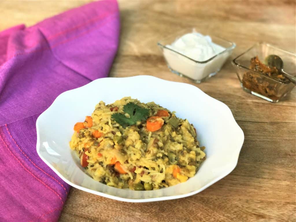 Khichdi with vegetables in a white bowl along with pickle and yogurt. 