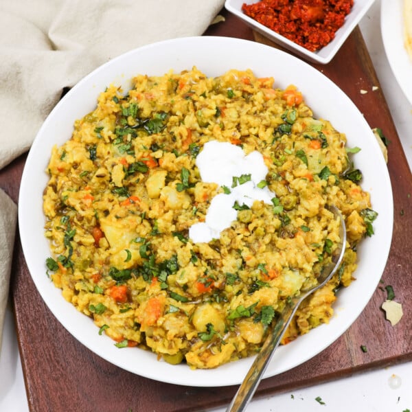 Masala khichdi in a white bowl topped with yogurt