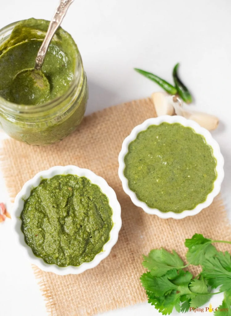Green cilantro mint chutney in two bowls and a glass jar. 