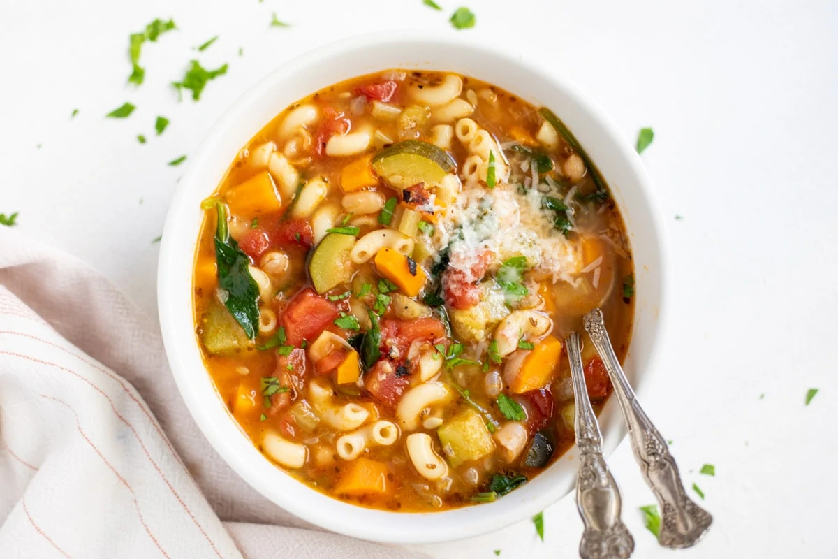 Minestrone soup with pasta and lots of vegetables in a white bowl