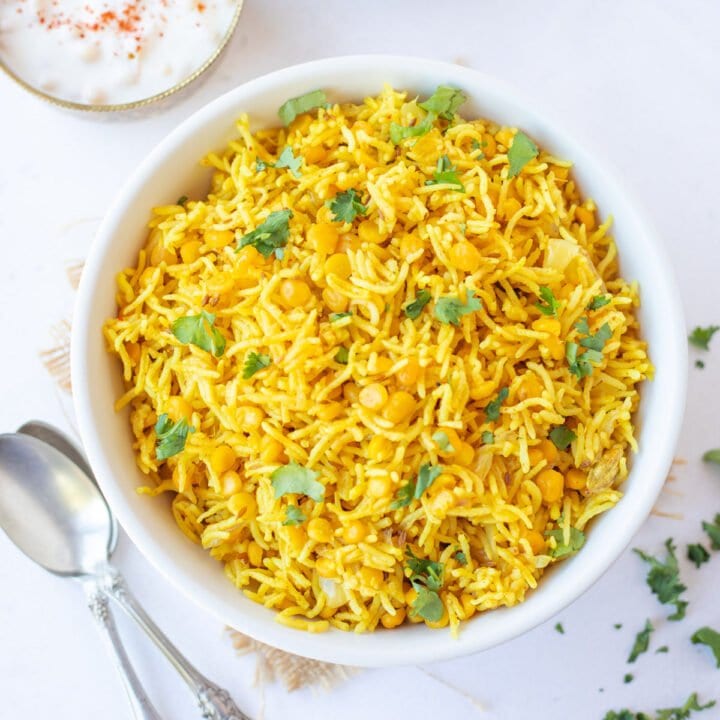 chana dal pulao in a white bowl with raita and onion salad on the side