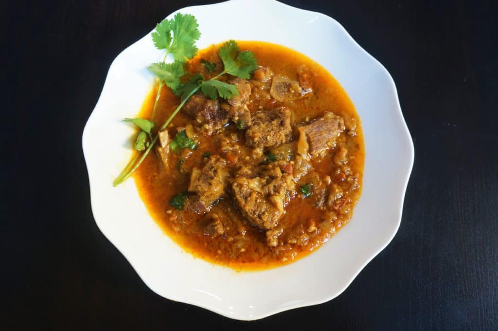 Goat Curry in a white plate with cilantro on side