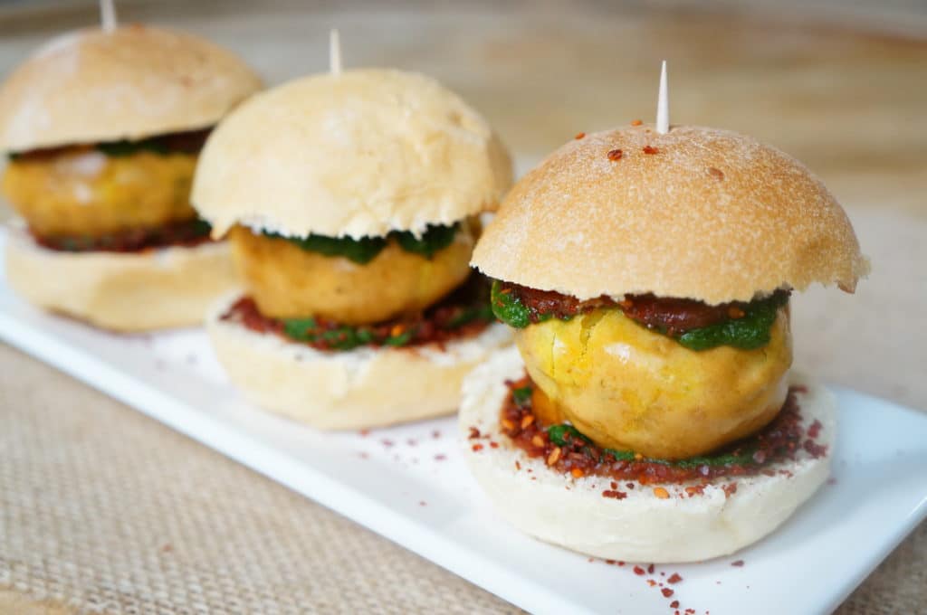 Potato Fritter Sliders, is a game day twist of the humble Mumbai street food, Vada Pav. A fried potato fritter is stuffed in between dinner rolls, along with sweet and spicy sauces or chutney