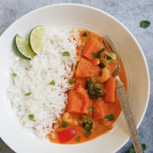 Thai Pumpkin curry with rice and sliced lime in a white plate