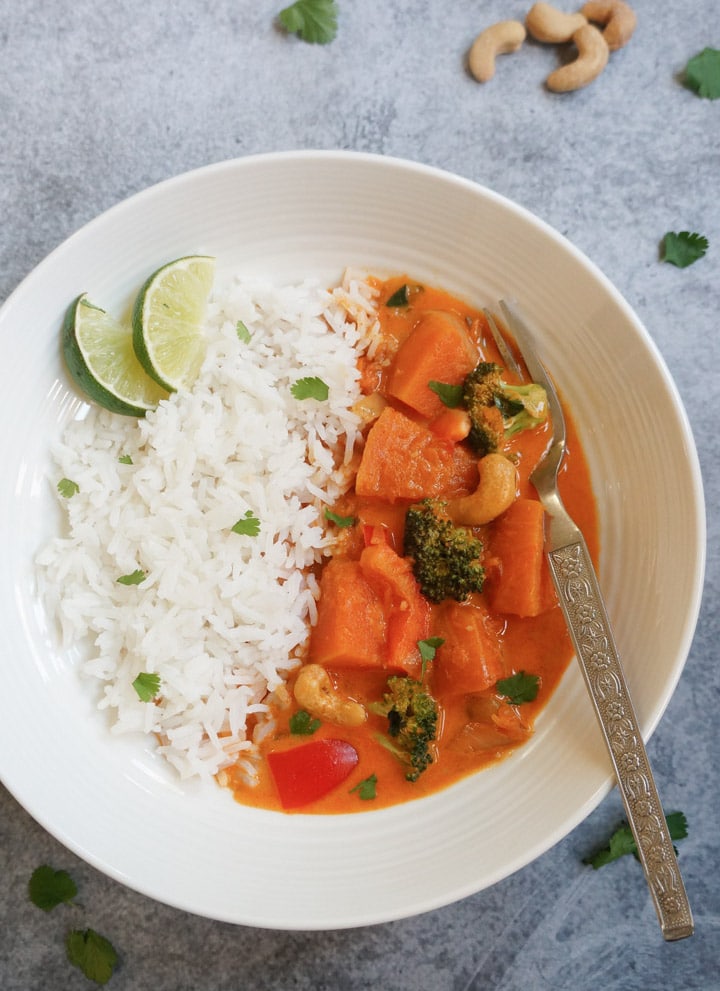 Thai Pumpkin curry with rice and sliced lime in a white plate
