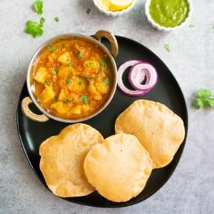 Potato Curry along with puffed bread (puri) and onions in a black plate
