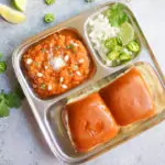Pav Bhaji served in a plate with onions and lime on the side