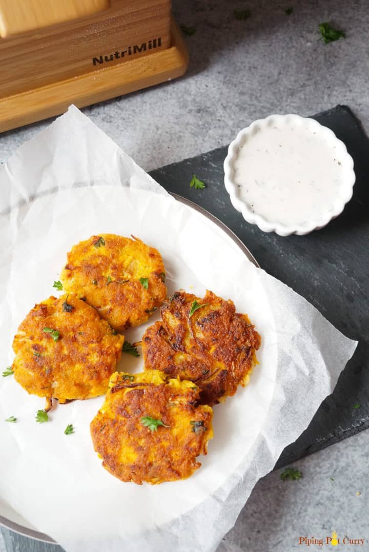 Vegan Chickpea Squash Fritters in a plate with yogurt dip on the side and Nutrimill Harvest in the back