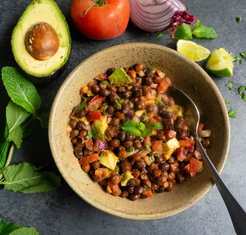 Kala Chana Chaat. Black Chickpea Salad in a bowl with avocado, tomato, onion, mint and lime pieces