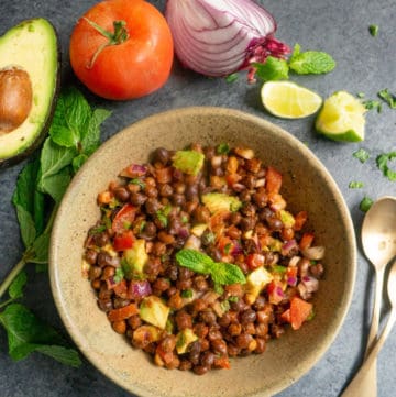 Kala Chana Chaat. Black Chickpea Salad in a bowl with avocado, tomato, onion, mint and lime pieces