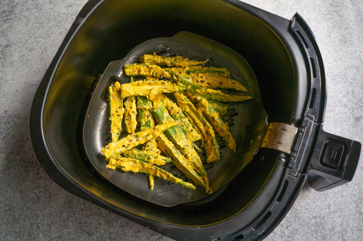 Slides okra covered in batter spread in air fryer grill pan