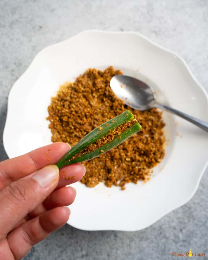 Okra stuffed with spices shown in hand with the spice mix in the back