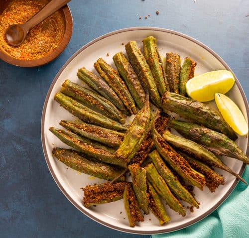 Bharwa Bhindi (Stuffed Okra) served in a plate with lemon wedges and the stuffed spices on the side.