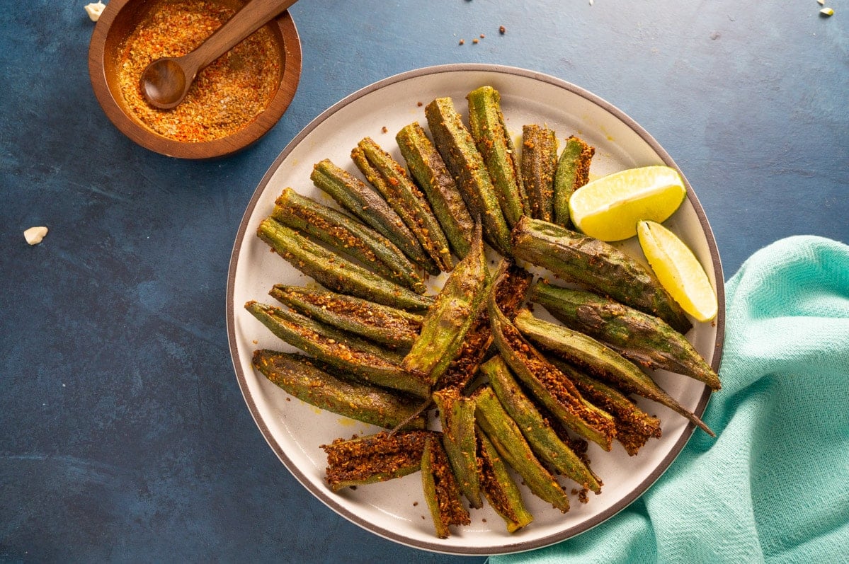 Bharwa Bhindi (Stuffed bhindi) served in a plate with lemon wedges and the stuffed spices on the side.