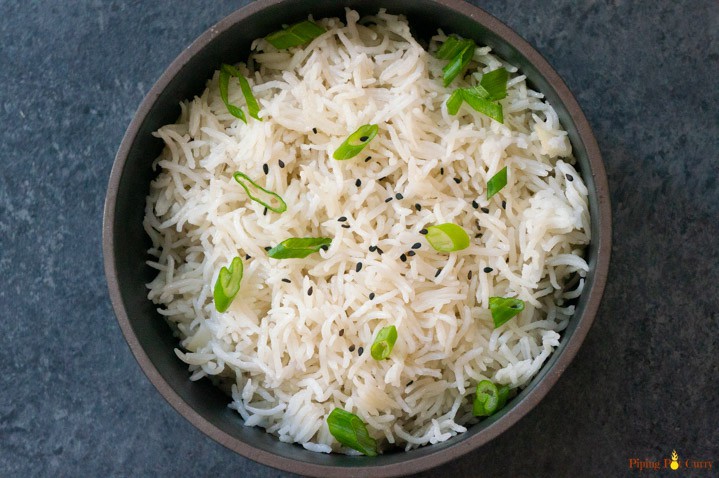 Coconut Rice made in the pressure cooker served in a black bowl topped with sesame seeds and scallions