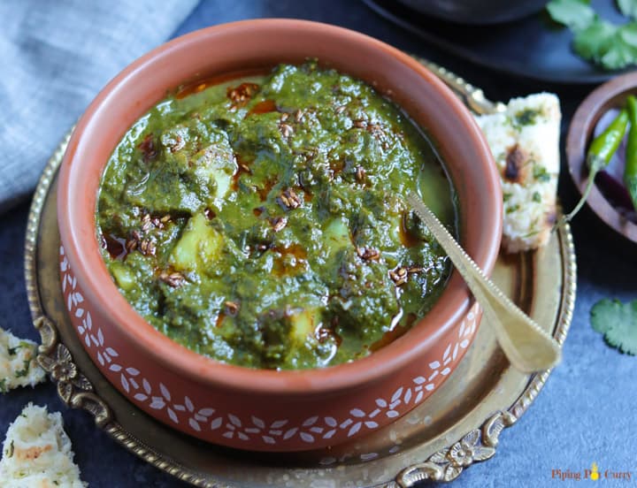 Saag Aloo made in the instant pot served in a earthen bowl with the tempering in the back and naan on the side.