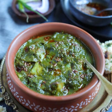 Saag Aloo made in the instant pot served in a earthen bowl with the tempering in the back and naan on the side.