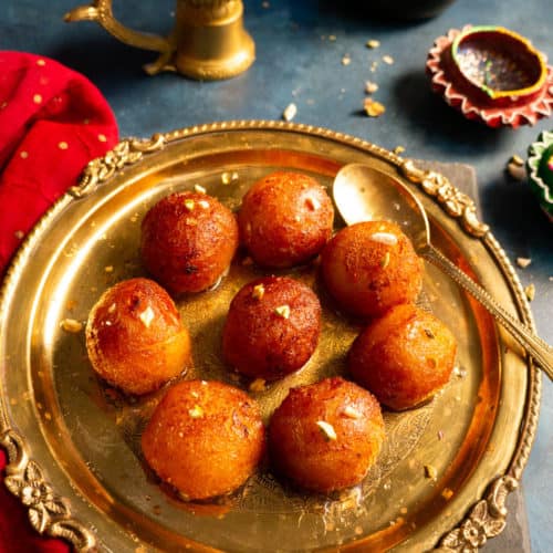 Gulab Jamun's served in a plate with some diya in the back for decoration