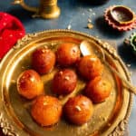 Gulab Jamun's served in a plate with some diya in the back for decoration
