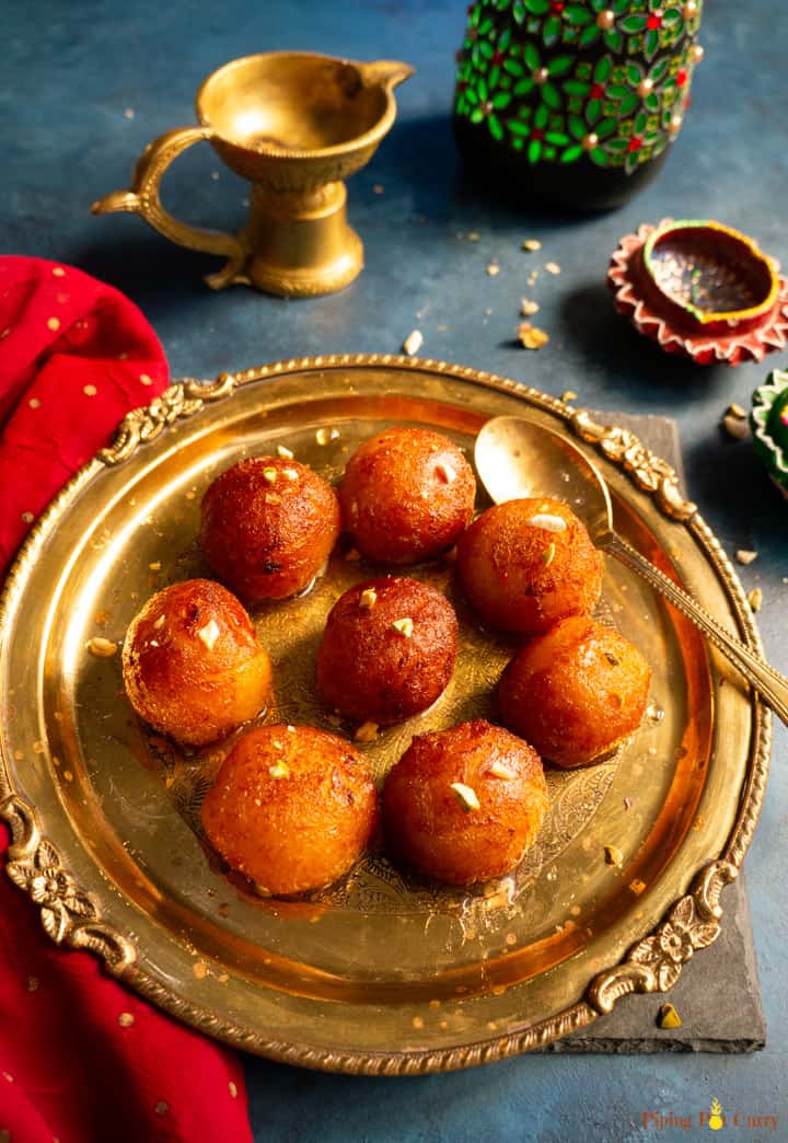 Gulab Jamun's served in a plate with some diya in the back for decoration