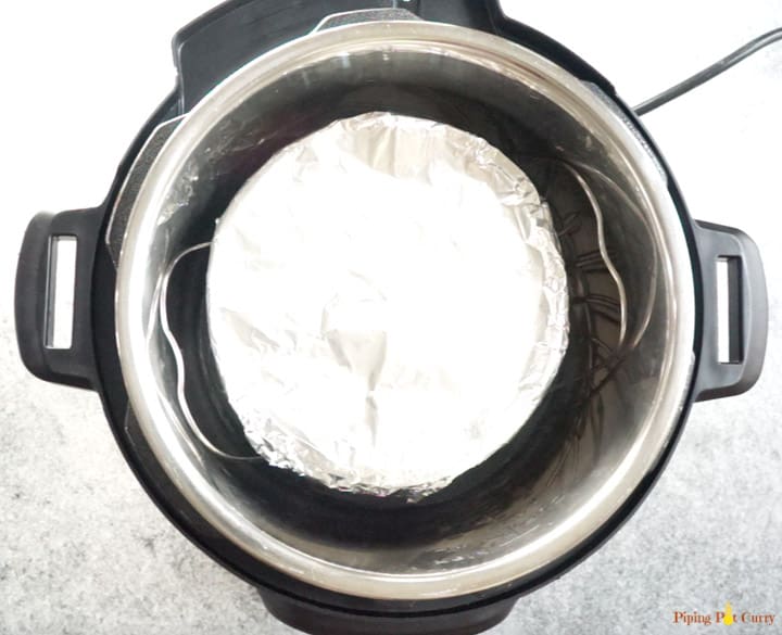 Cake pan filled with brownie batter and covered with foil placed on a trivet to make instant pot brownies