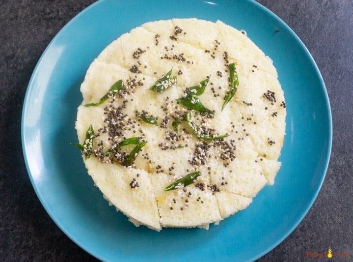 Rava Dhokla Instant Pot - Piping Pot Curry-11 Tempering added to Sooji Dhokla on a blue plate