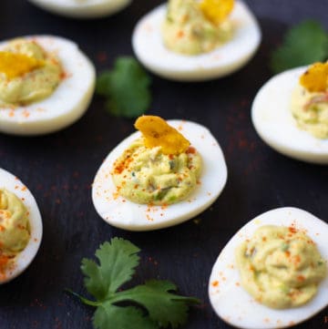 Guacamole Deviled Eggs on a black platter garnished with paprika and a tortilla chip