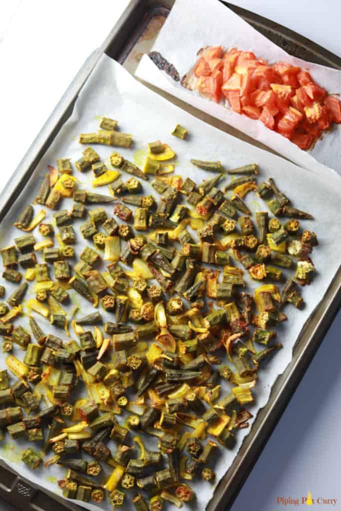 Oven Roasted Okra with onions and tomatoes laid out in a sheet pan. 