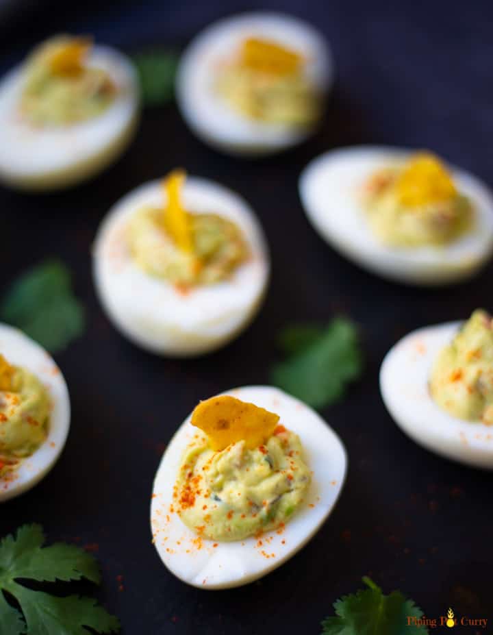 Guacamole Deviled Eggs on a black platter garnished with paprika and a tortilla chip