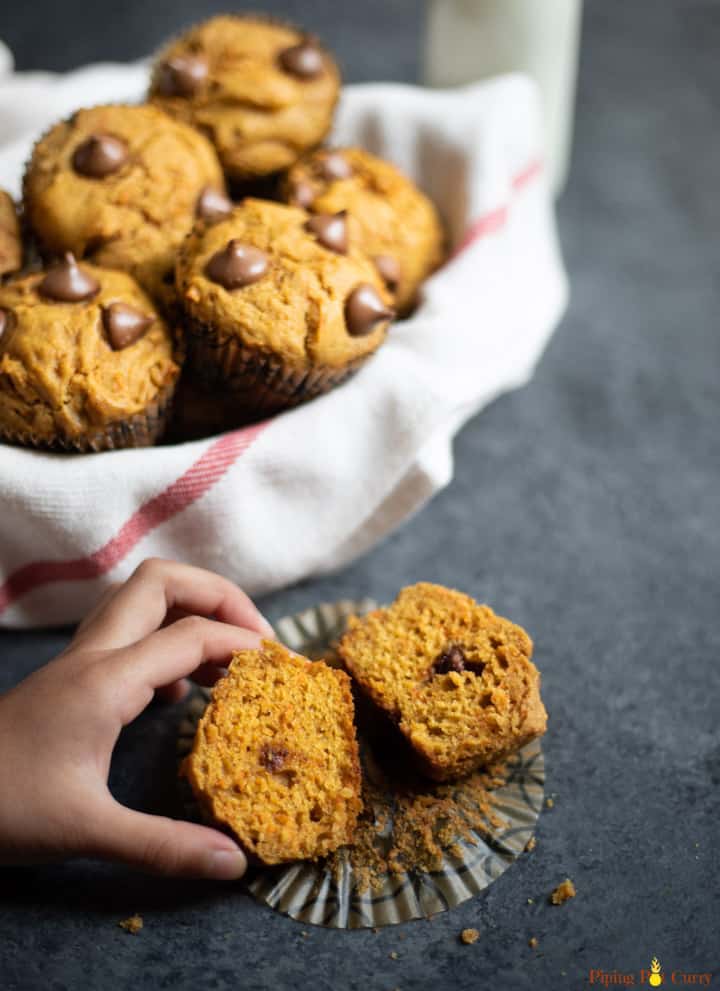Healthy Whole Wheat Carrot Muffin cut into two pieces being picked up, along with a basket of muffins.