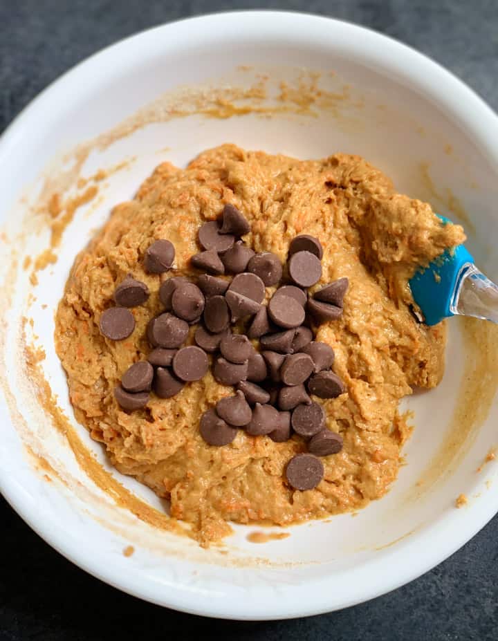 Mix dry & wet ingredients and add chocolate chips to make carrot muffins in a white bowl
