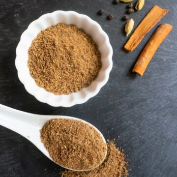 Chai Masala Spice Mix in a white bowl and spoon along with some whole spices