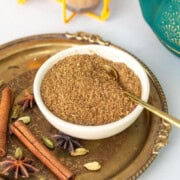 Chai masala powder in a bowl with whole spices spread around