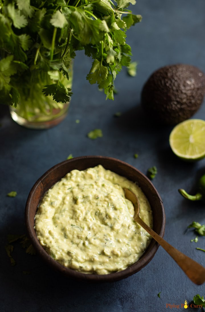 avocado cilantro sauce in a wooden bowl and cilantro leaves, avocado and slice lime on top