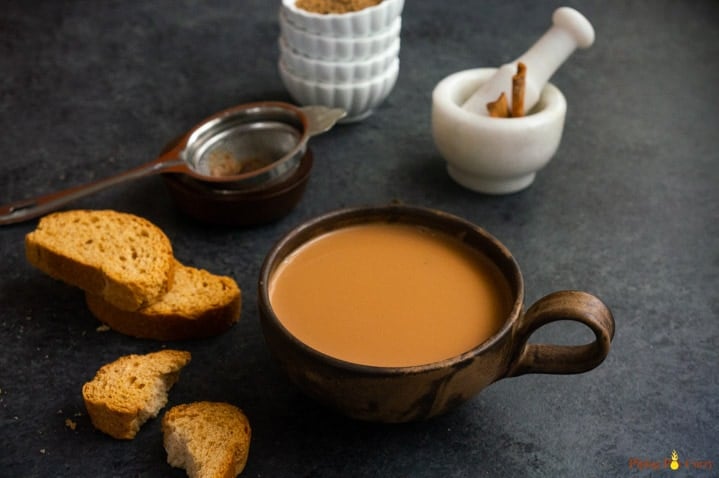 Tea in a cup with toast on the side and mortar pestle, strainer in the back